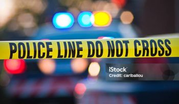 Shallow depth of field image taken of yellow law enforcement line with police car and lights in the background.